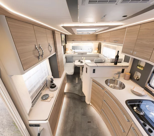 Innenraum des Dethleffs Alpa A 7820-2 Wohnmobils: elegante Küche mit Edelstahlspüle und Gasherd, großzügige Sitzgruppe, hochwertige Holzoptik und helle LED-Beleuchtung für erstklassigen Wohnkomfort unterwegs.